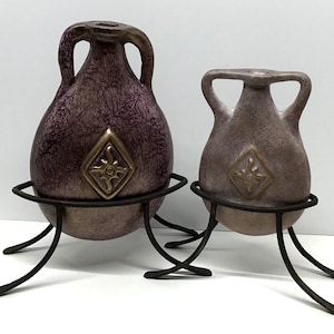 May include: Two decorative ceramic vases with a purple and gold glaze, each with a gold design on the front, sitting on black metal stands.