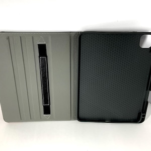 May include: Gray tablet case, open to display the interior. The left side is gray with a black elastic strap. The right side is black with a honeycomb pattern. The case is designed to protect a tablet.