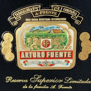 May include: An Arturo Fuente cigar label with gold accents and text. The label features a landscape scene with lions, the text "ARTURO FUENTE", and the words "Reserva Superior Limitada". Several gold coins are also visible.