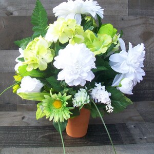 May include: A white and green artificial flower arrangement in a terracotta pot. The arrangement features white dahlias, white daisies, and green hydrangeas.