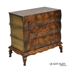 May include: A three-drawer chest of drawers designed to resemble a stack of books. The furniture piece has a brown and gold finish, with curved edges and ornate legs. The chest is a unique decorative item.