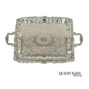 May include: A rectangular silver serving tray with ornate floral and scrollwork detailing. The tray has two handles and a decorative border. The text "QUALITY IS KEY decor" is printed in black at the bottom right.