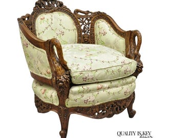 May include: An antique armchair with a carved wooden frame and floral patterned upholstery. The chair features ornate details, including carved armrests and back supports. The cushions are light green with a delicate pink floral design. A classic piece of furniture.