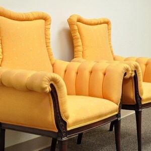 May include: A pair of yellow upholstered armchairs with tufted backs and rolled arms. The chairs have wooden frames and legs.