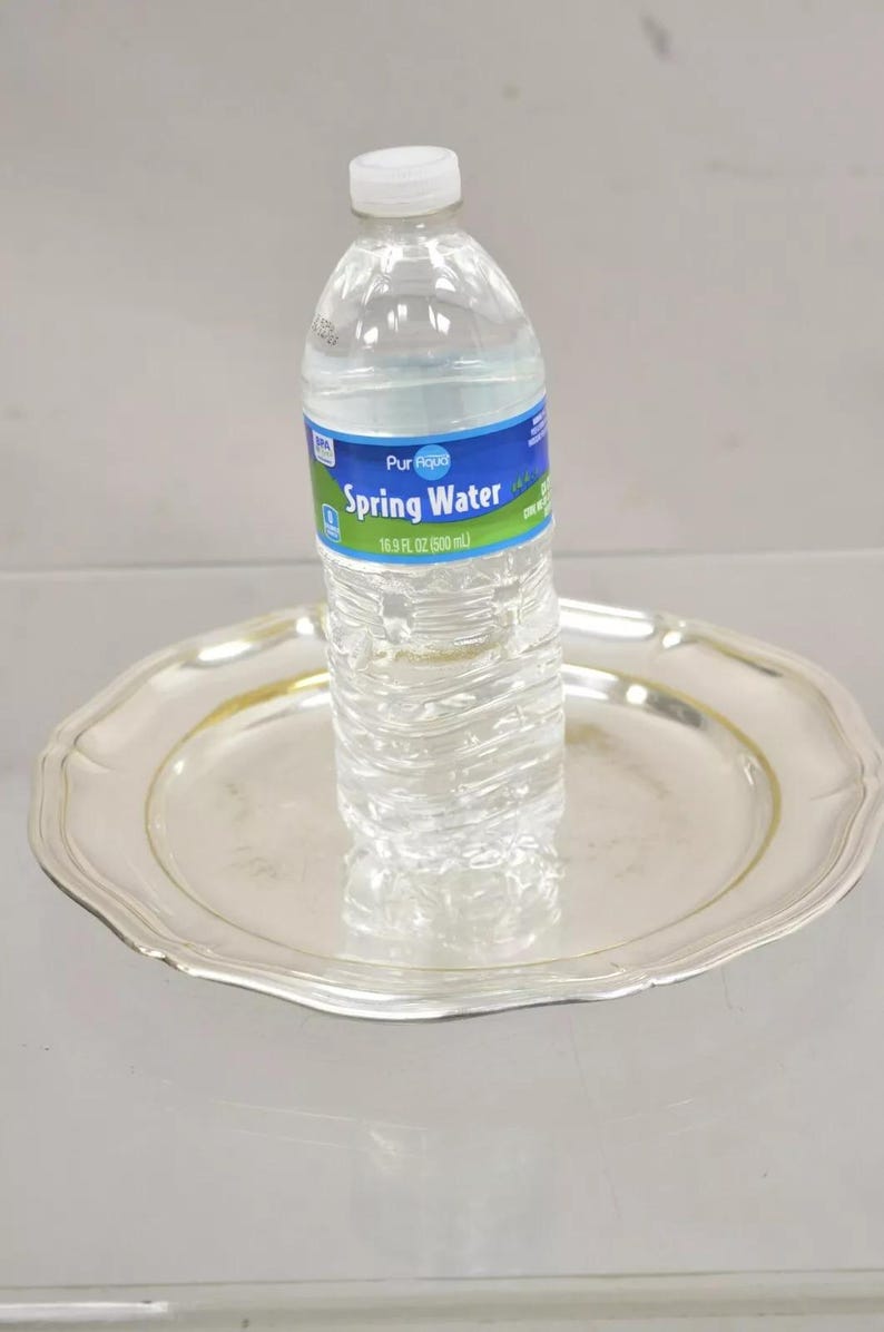 Puede incluir: Una botella de pl&aacute;stico transparente de agua de manantial Pur Aqua sobre una bandeja de plata. La botella es de 500 ml.