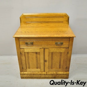 May include: Antique oak wood cabinet with a single drawer and two doors. The cabinet has a decorative top with a raised panel and a simple design.