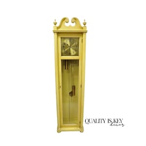 May include: A yellow wooden grandfather clock with a glass door revealing the clock's inner workings. The clock face has black Roman numeral markings and a gold-colored center.