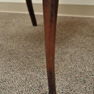 May include: Close-up of a dark brown wooden chair leg with a slightly rounded bottom.