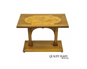 May include: A wooden end table with a rectangular top and a lower shelf. The top is made of a light wood with a darker wood inlay in the shape of an oval. The table has a simple, elegant design.