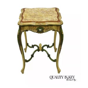 May include: A small, square, antique end table with a floral patterned top. The table is painted in a cream color with green accents and has ornate, curved legs.