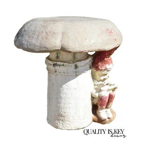 May include: A whimsical garden gnome statue under a mushroom-shaped structure. The mushroom top is off-white, and the gnome wears a red hat and boots. The base is white with the text "QUALITY IS KEY decor".
