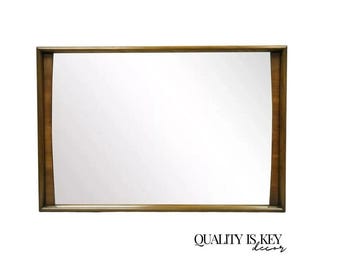 May include: A large, rectangular mirror with a wood frame. The frame has a curved design on the top and bottom edges. The mirror is reflecting a white wall.