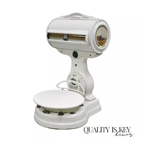 May include: An antique white scale with a round platform and a curved display. The scale has a large, circular dial and a decorative top with text. The base is ornate, and the overall design is vintage.