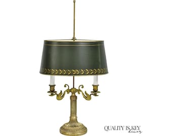 May include: An antique brass table lamp with a dark green lampshade. The shade is adorned with a gold leaf pattern and a gold trim. The lamp has two candle holders and a decorative base. The text "QUALITY IS KEY decor" is visible.