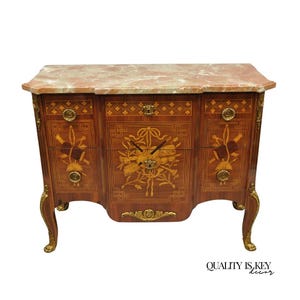 May include: A wooden chest of drawers with a marble top. The chest has three drawers and is decorated with inlaid wood designs and gold-colored hardware. The legs are curved and also have gold accents. The chest is a rich brown color.