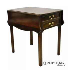 May include: A dark brown wooden end table with two drawers and a drop-leaf top. The table has a curved design and gold-toned hardware.