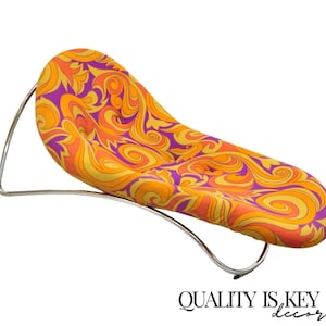 May include: A chrome-framed chaise lounge with a colorful, psychedelic patterned fabric. The fabric features swirls and abstract shapes in shades of orange, yellow, and purple.