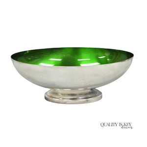 May include: A silver-toned pedestal bowl featuring a vibrant, glossy emerald green interior. The exterior has a smooth, metallic finish, and the bowl rests on a circular base. The text "QUALITY IS KEY decor" is printed in the bottom right corner.