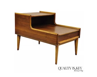 May include: Mid-century modern end table with a unique angled design. The table is made of wood with a rich brown finish and features a lower shelf and a drawer. The table has four tapered legs.