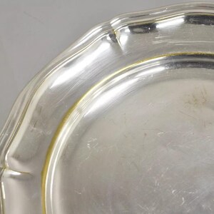 Puede incluir: Un plato de servir de plata con un borde festoneado y un borde dorado.