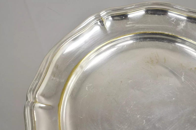 Puede incluir: Un plato de servir de plata con un borde festoneado y un borde dorado.