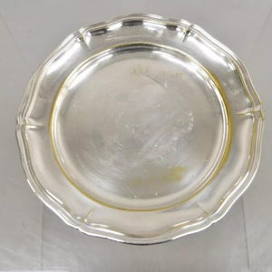 Puede incluir: Un plato de servir de plata con un borde elevado y un borde ligeramente festoneado. El plato tiene un acabado brillante y pulido.