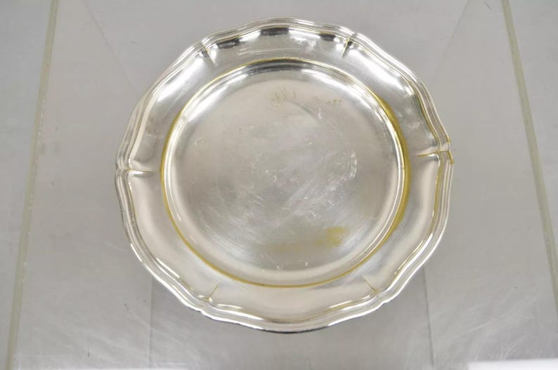 Puede incluir: Un plato de servir de plata con un borde elevado y un borde ligeramente festoneado. El plato tiene un acabado brillante y pulido.