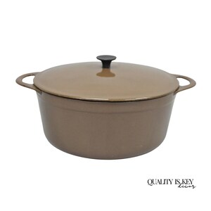 May include: A brown cast iron Dutch oven with a matching lid and black handle. The pot has two side handles for easy carrying. The text "QUALITY IS KEY decor" is in the bottom right corner.