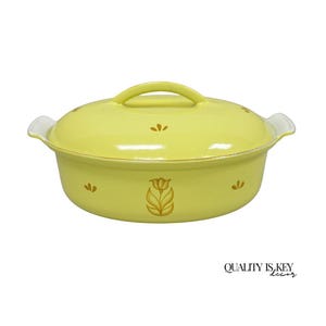 May include: A yellow oval casserole dish with a lid and handles. The dish has a floral design and the text "QUALITY IS KEY decor" at the bottom. The dish is likely made of ceramic or porcelain.