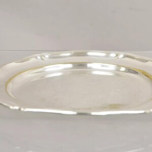 Puede incluir: Una fuente de servir de plata con un borde festoneado. La fuente es redonda y tiene una superficie lisa y reflectante.