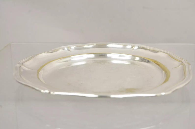 Puede incluir: Una fuente de servir de plata con un borde festoneado. La fuente es redonda y tiene una superficie lisa y reflectante.