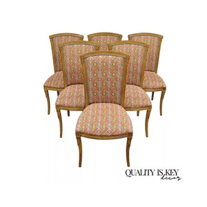 May include: Set of seven wooden dining chairs. The chairs have a light brown frame and a patterned fabric seat and backrest in shades of orange, pink, and gray. The chairs have curved legs and a decorative top.