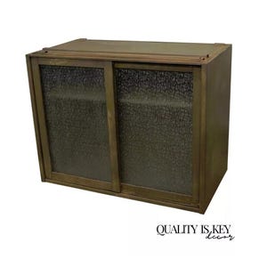 May include: A vintage brass cabinet with two sliding glass doors. The glass has a textured, bubbled pattern. The cabinet has a dark brown finish.