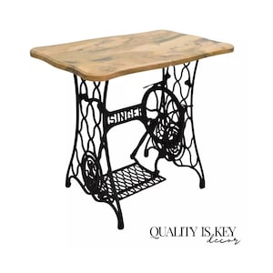 May include: A black metal Singer sewing machine base repurposed as a table with a light wood top. The table has a shelf underneath.