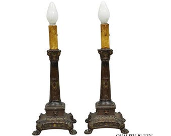 May include: Pair of antique-style electric candle holders. Each candle holder features a brown, ornate base with decorative details, a brown column, and a faux candle with a white bulb. The candle holders are designed to resemble vintage decor.
