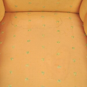 May include: Close-up of a light orange chair with a tufted back and seat. The fabric has a subtle pattern of small green four-leaf clover designs.