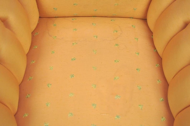 May include: Close-up of a light orange chair with a tufted back and seat. The fabric has a subtle pattern of small green four-leaf clover designs.