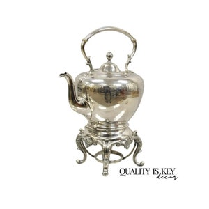 May include: A silver teapot with a stand. The teapot has a round body and a curved spout. The stand has three legs and is decorated with ornate details.