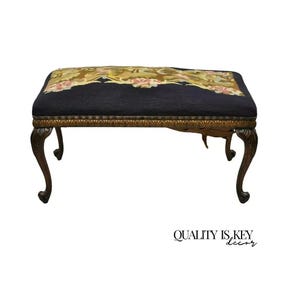 May include: A vintage wooden bench with a dark blue upholstered seat and a floral patterned tapestry top. The bench has ornate carved legs.