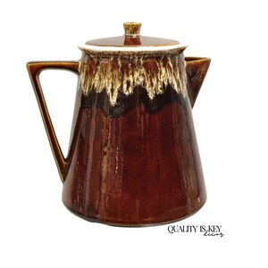 May include: A brown glazed ceramic coffee pot with a white rim and a brown lid. The pot has a brown and white glaze pattern.