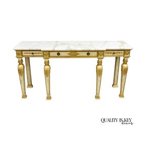 May include: An antique desk with a white marble top and cream-colored frame. The desk features gold accents, including drawer pulls and decorative carvings on the legs. The desk has two drawers and is a classic piece of furniture.