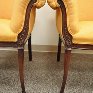 May include: A pair of yellow upholstered chairs with wooden frames and carved details. The chairs have a scrolled back and a curved armrest.