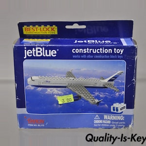 May include: A blue and white box with a jetBlue airplane construction toy inside. The box has the words "jetBlue construction toy" on it. The toy is made of gray plastic blocks and has a blue tail fin with the jetBlue logo. The box also has a warning label about choking hazards.