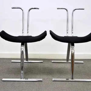 May include: Two chrome and black upholstered chairs with a unique design. The chairs have a curved back and a wide base.