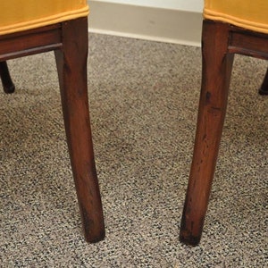 May include: Close-up of the legs of two chairs with a dark wood finish and a yellow fabric seat.