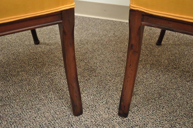 May include: Close-up of the legs of two chairs with a dark wood finish and a yellow fabric seat.