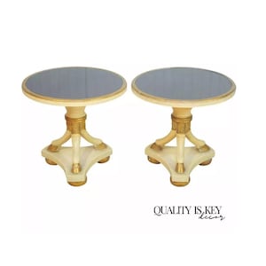 May include: A pair of round, white end tables with gold accents. Each table has a black glass top and a three-legged base with gold paw feet.