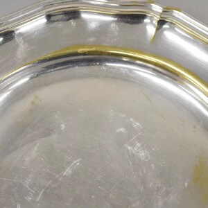 Puede incluir: Un plato de servir de plata con un borde dorado. El plato tiene un borde festoneado y una superficie lisa y reflectante.