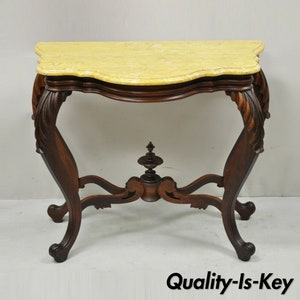 May include: A vintage, ornately carved wooden console table with a scalloped, cream-colored marble top.