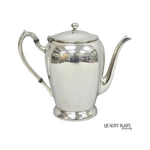 May include: A silver-colored teapot with a curved handle and a long, slender spout. The teapot has a lid with a small knob on top. The base of the teapot is slightly flared. The words "QUALITY IS KEY decor" are printed in black on the bottom right.